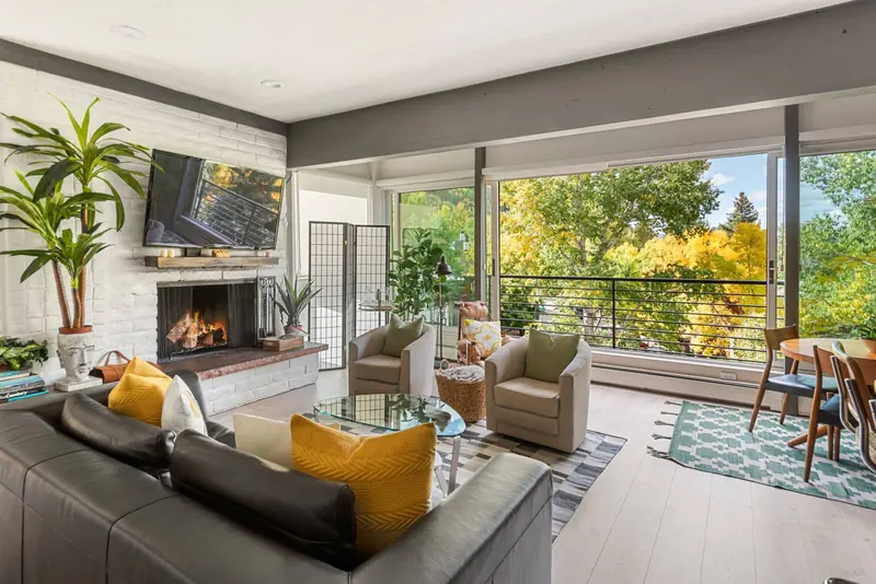 Top-floor living room of The Galena Penthouse at Durant 6D: the wood-burning fireplace and floor-to-ceiling windows onto Aspen Mountain's autumn gold.